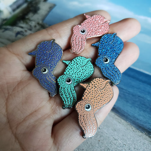 A hand holding all five color variants of the squid pin